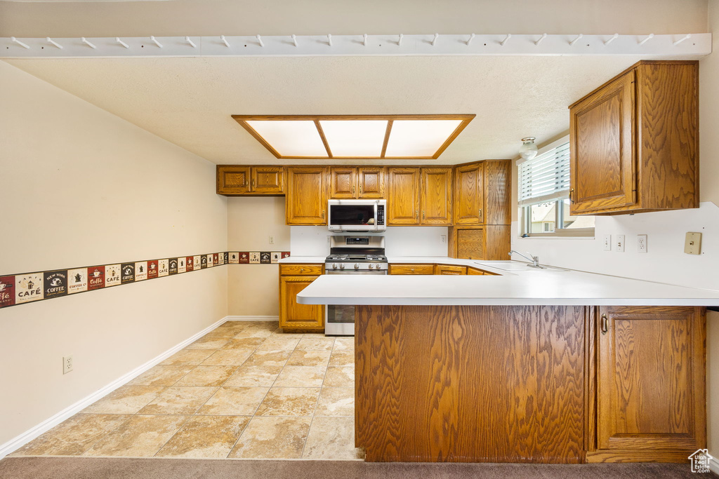 Kitchen with baseboards, a peninsula, brown cabinets, appliances with stainless steel finishes, and a sink