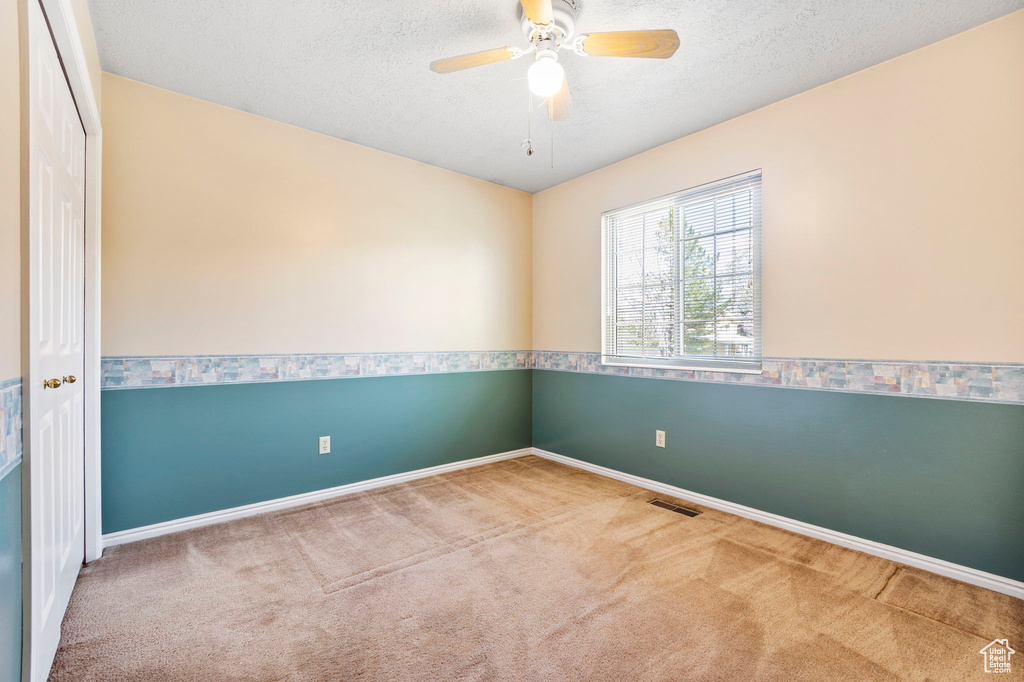 Carpeted spare room with baseboards, ceiling fan, and a textured ceiling