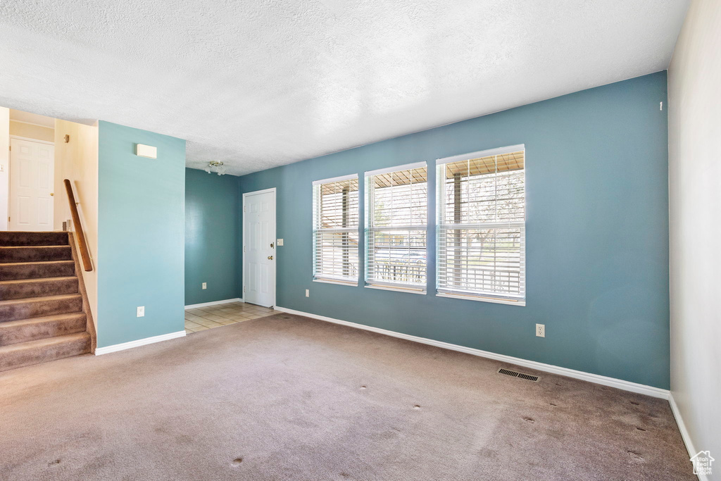 Unfurnished living room with stairway, a textured ceiling, visible vents, and carpet floors