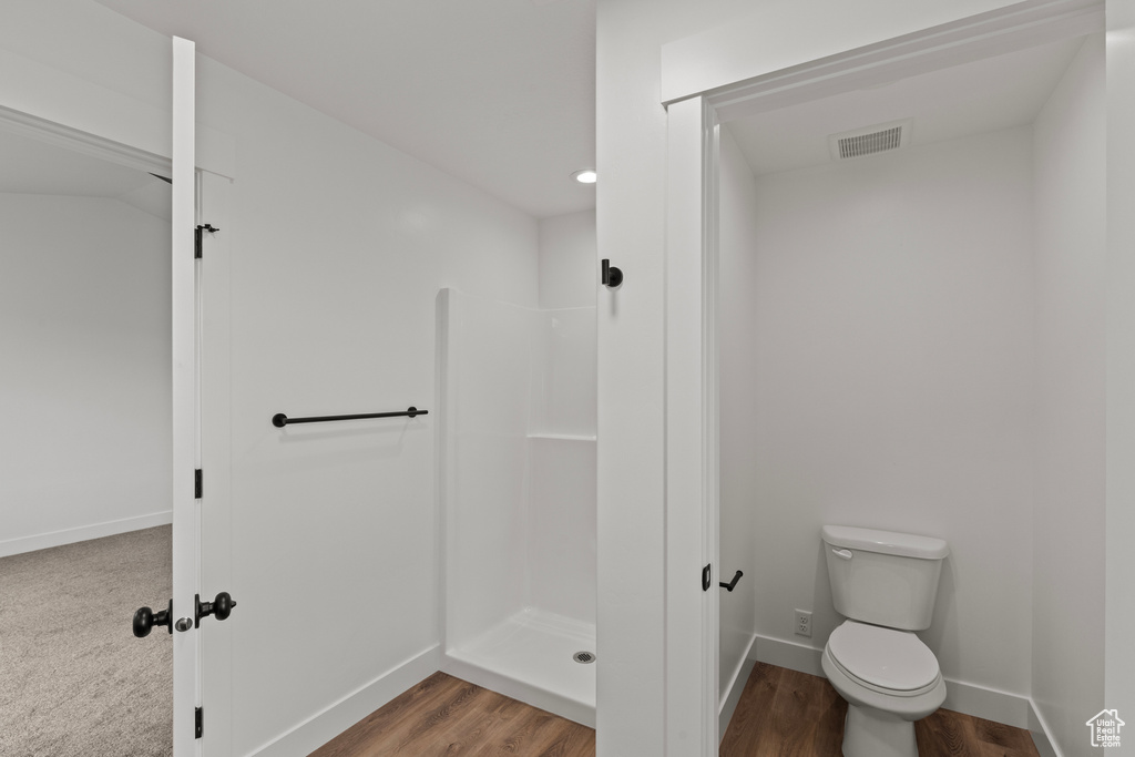 Bathroom featuring walk in shower, toilet, baseboards, and wood finished floors