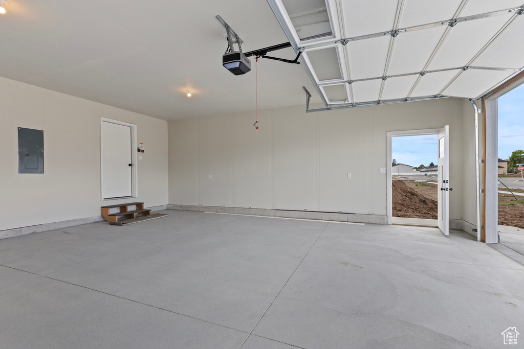 Garage featuring electric panel, a garage door opener, and baseboards