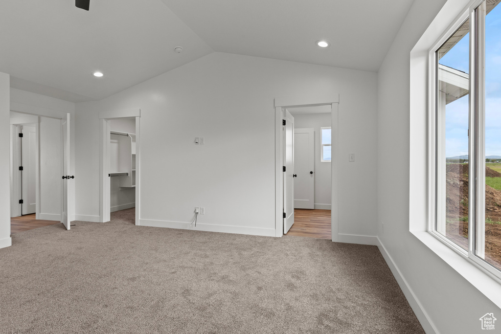 Unfurnished bedroom featuring multiple windows, carpet floors, baseboards, lofted ceiling, and a walk in closet