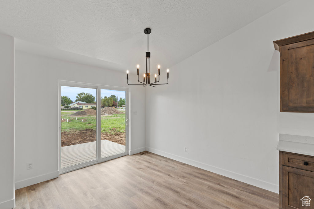 Unfurnished dining area with a chandelier, light wood-type flooring, and baseboards