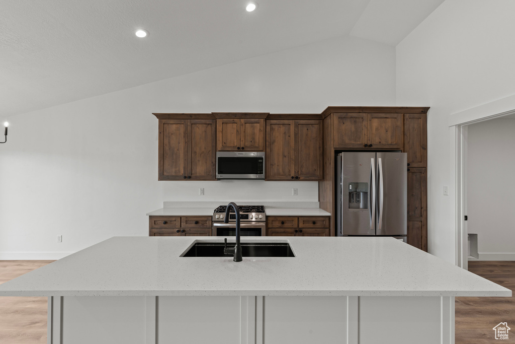 Kitchen featuring appliances with stainless steel finishes, lofted ceiling, a sink, light wood-style floors, and a kitchen island with sink