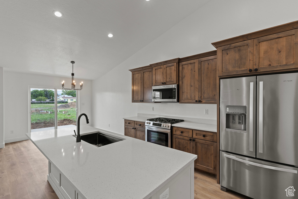 Kitchen with stainless steel appliances, a sink, vaulted ceiling, a chandelier, and light wood finished floors