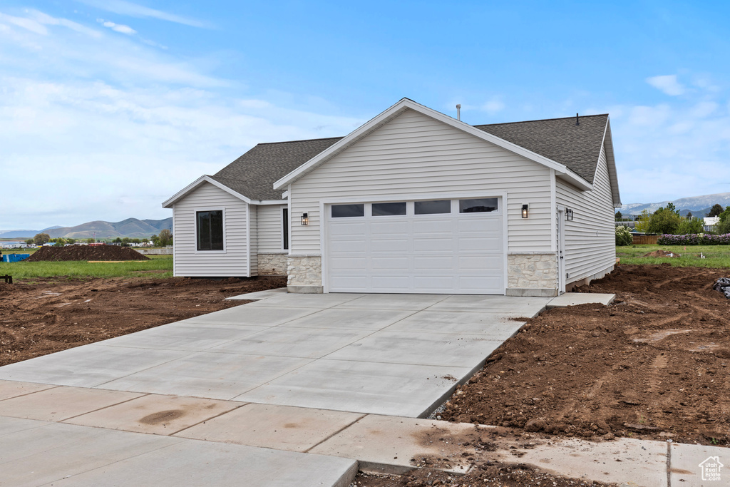 Ranch-style house with a shingled roof, stone siding, a garage, driveway, and a mountain view