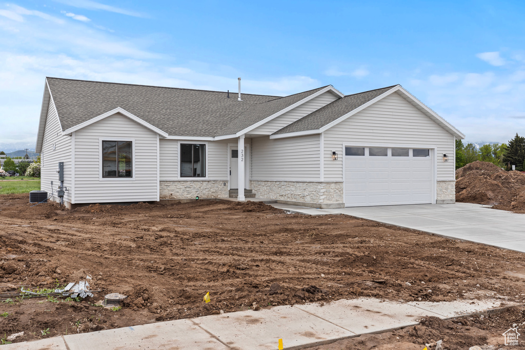 Single story home with stone siding, a shingled roof, an attached garage, concrete driveway, and cooling unit