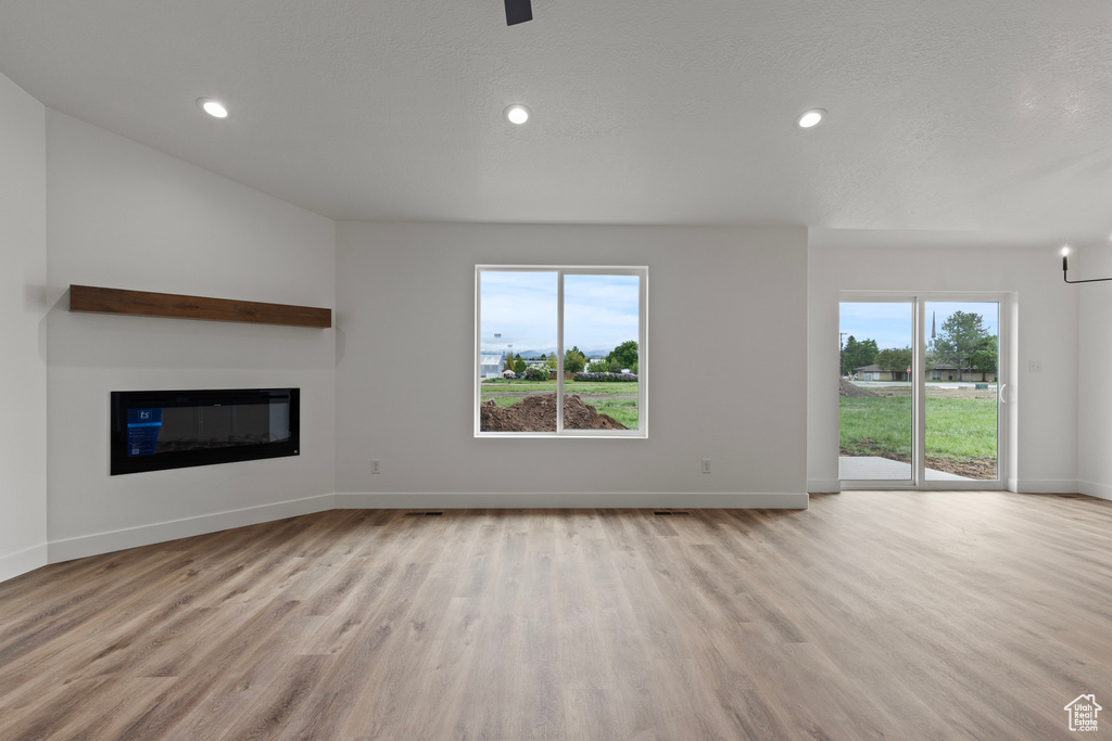 Unfurnished living room with wood finished floors, baseboards, a glass covered fireplace, and recessed lighting