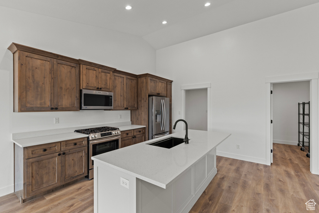 Kitchen featuring appliances with stainless steel finishes, a sink, high vaulted ceiling, a kitchen island with sink, and light wood-style floors
