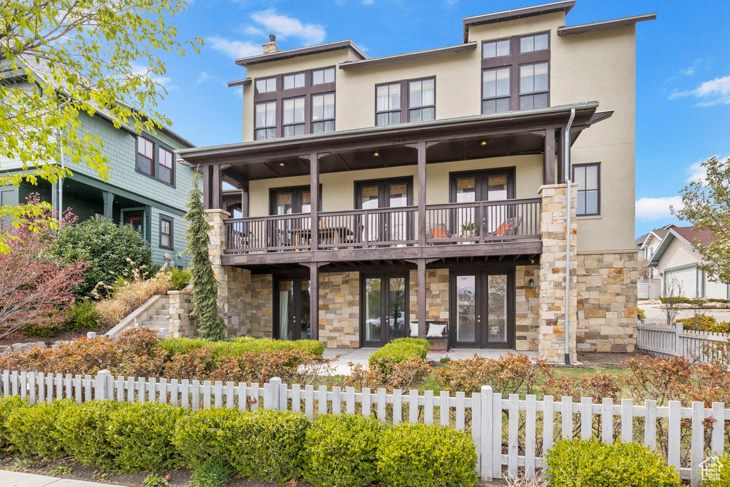 View of front of home with french doors, a fenced front yard, stucco siding, and stone siding