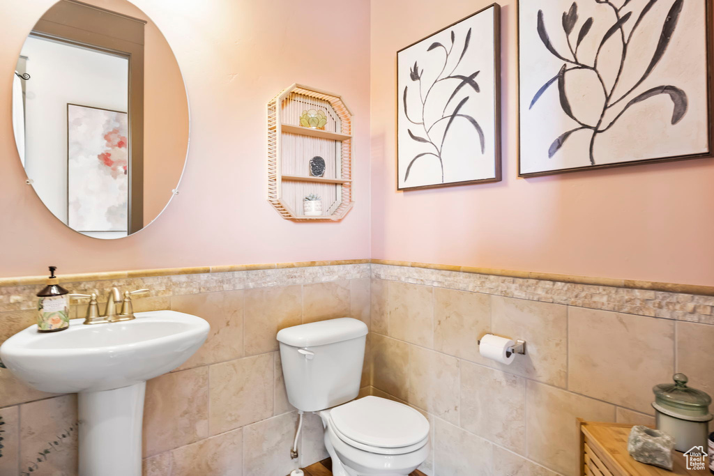 Half bathroom with toilet, tile walls, and a wainscoted wall