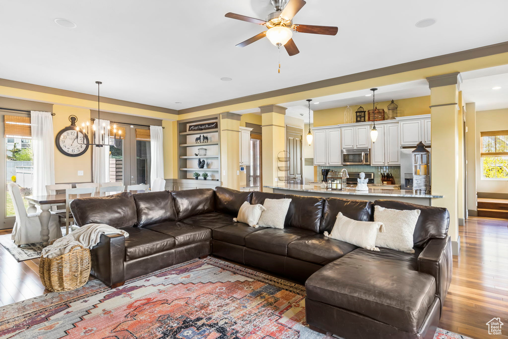 Living room featuring decorative columns, light wood-style floors, and ceiling fan with notable chandelier
