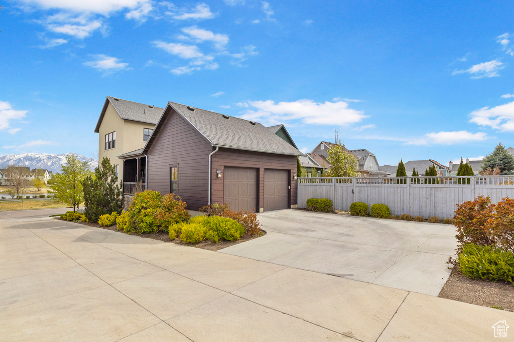 View of side of property featuring an attached garage, a residential view, concrete driveway, and fence