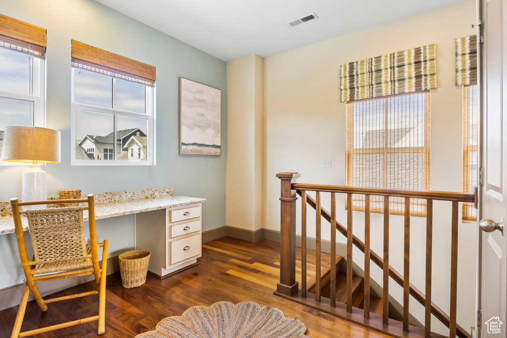 Office space with dark wood-style flooring, visible vents, baseboards, and built in desk