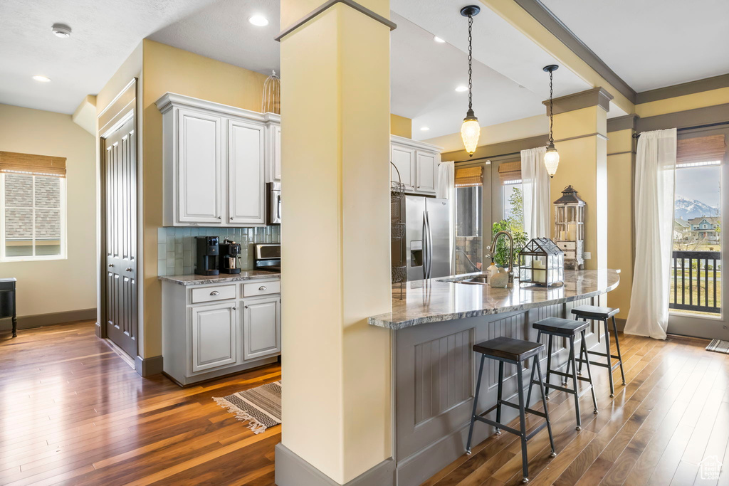 Kitchen featuring stainless steel fridge with ice dispenser, a breakfast bar, light stone countertops, dark wood-type flooring, and a sink
