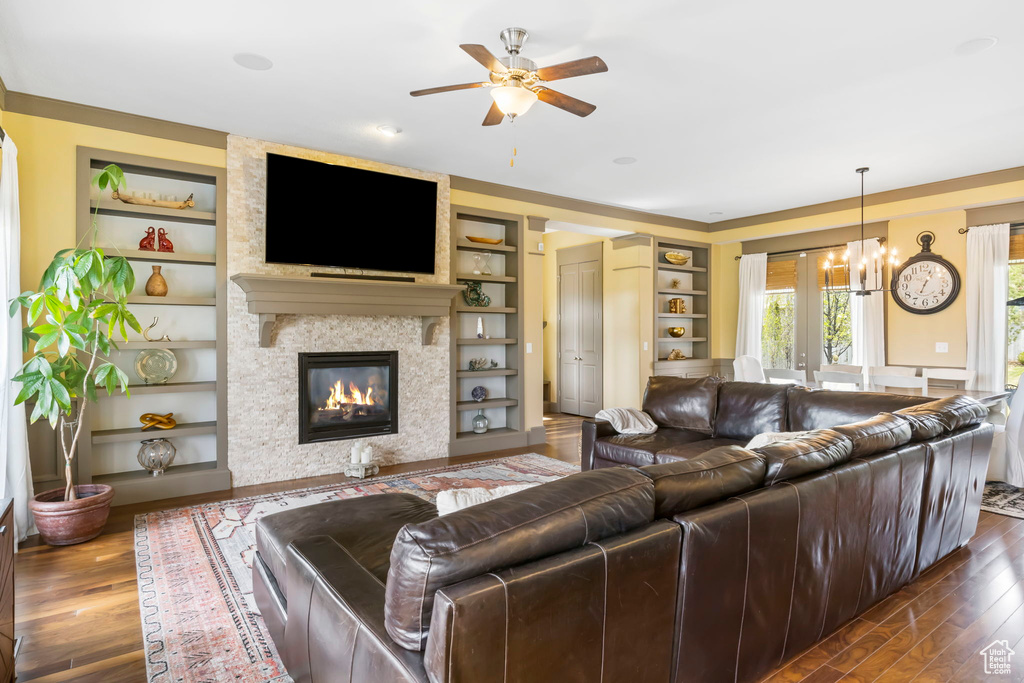 Living area featuring ceiling fan with notable chandelier, dark wood-style flooring, a fireplace, and built in shelves
