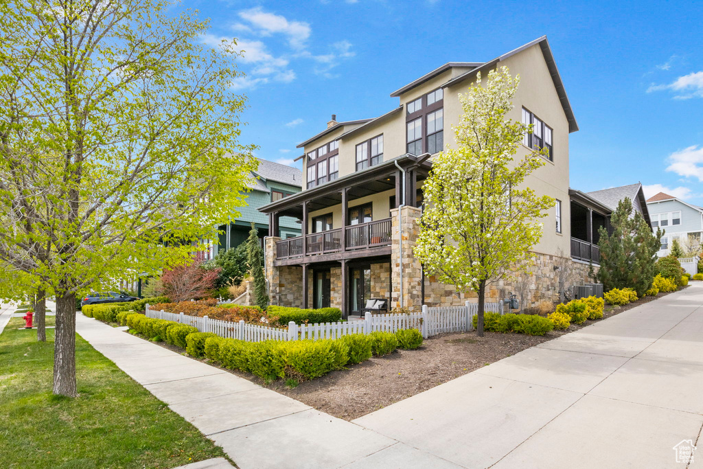 Exterior space featuring a fenced front yard, stucco siding, stone siding, a balcony, and central AC unit