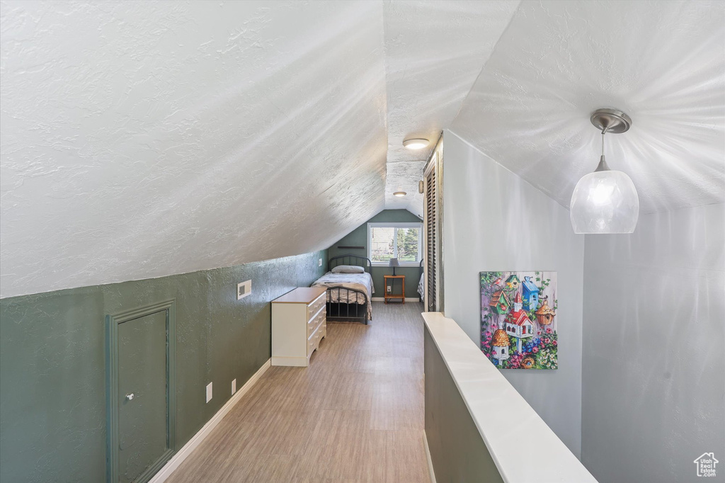Bonus room featuring baseboards, a textured wall, a textured ceiling, lofted ceiling, and wood finished floors