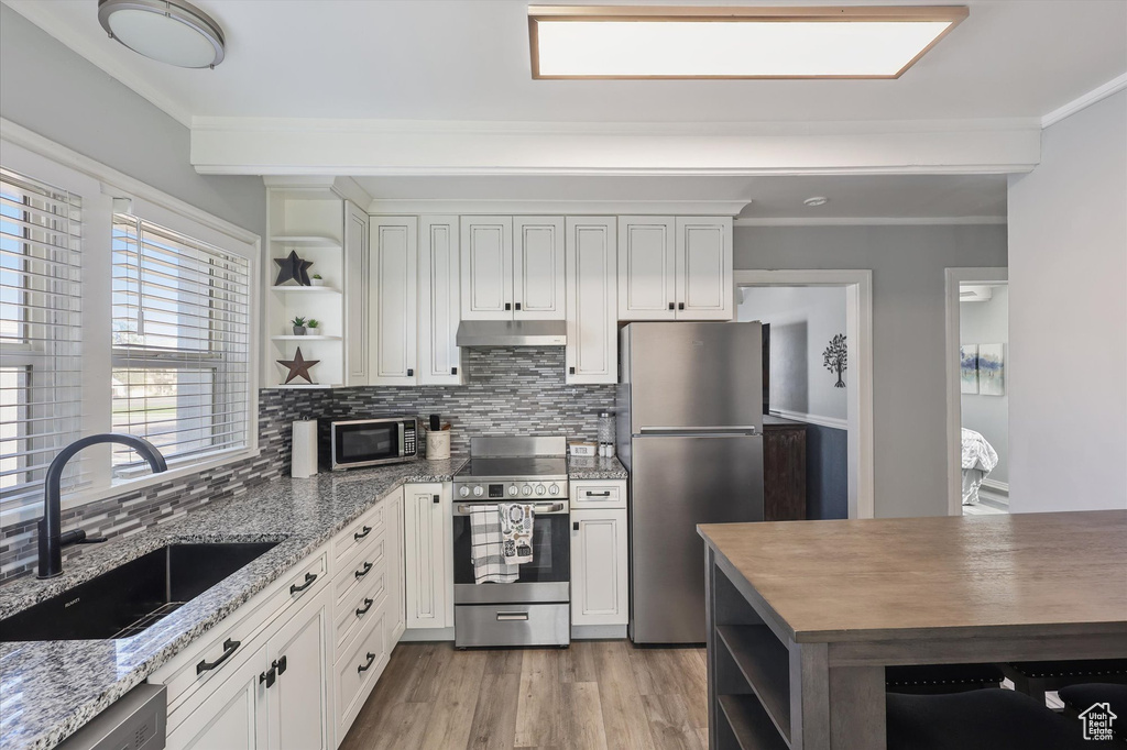 Kitchen featuring open shelves, a sink, appliances with stainless steel finishes, under cabinet range hood, and crown molding