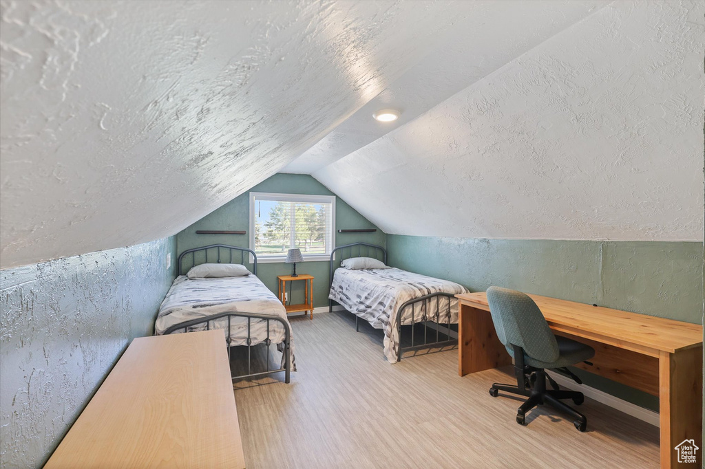 Bedroom featuring a textured wall, a textured ceiling, vaulted ceiling, and wood finished floors