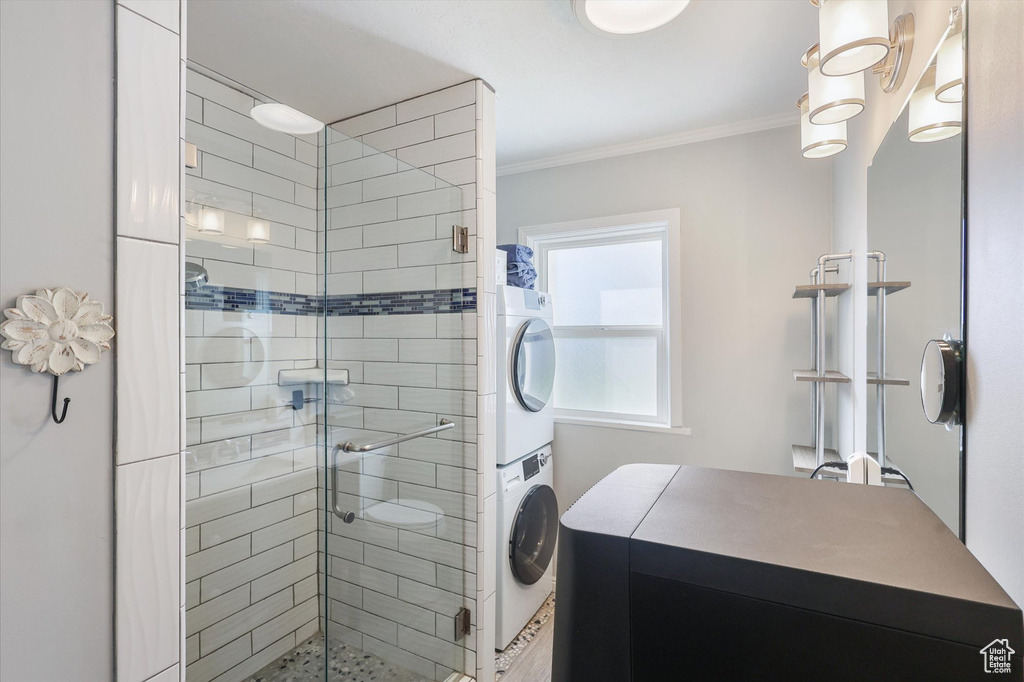 Bathroom featuring ornamental molding, stacked washer and clothes dryer, and a stall shower