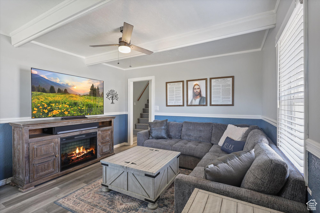 Living area with ceiling fan, a lit fireplace, beam ceiling, and wood finished floors