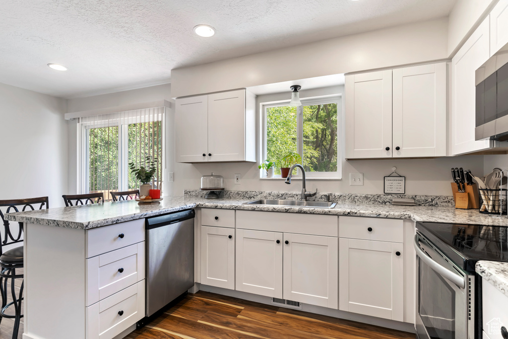 Kitchen with a breakfast bar, a peninsula, white cabinetry, appliances with stainless steel finishes, and a sink
