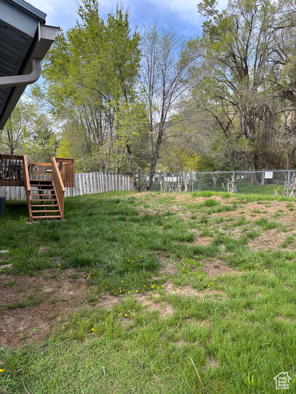 View of yard with fence, a wooden deck, and stairway