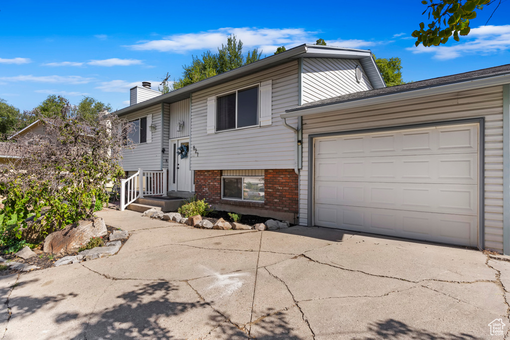 Split foyer home with concrete driveway, brick siding, a chimney, and an attached garage