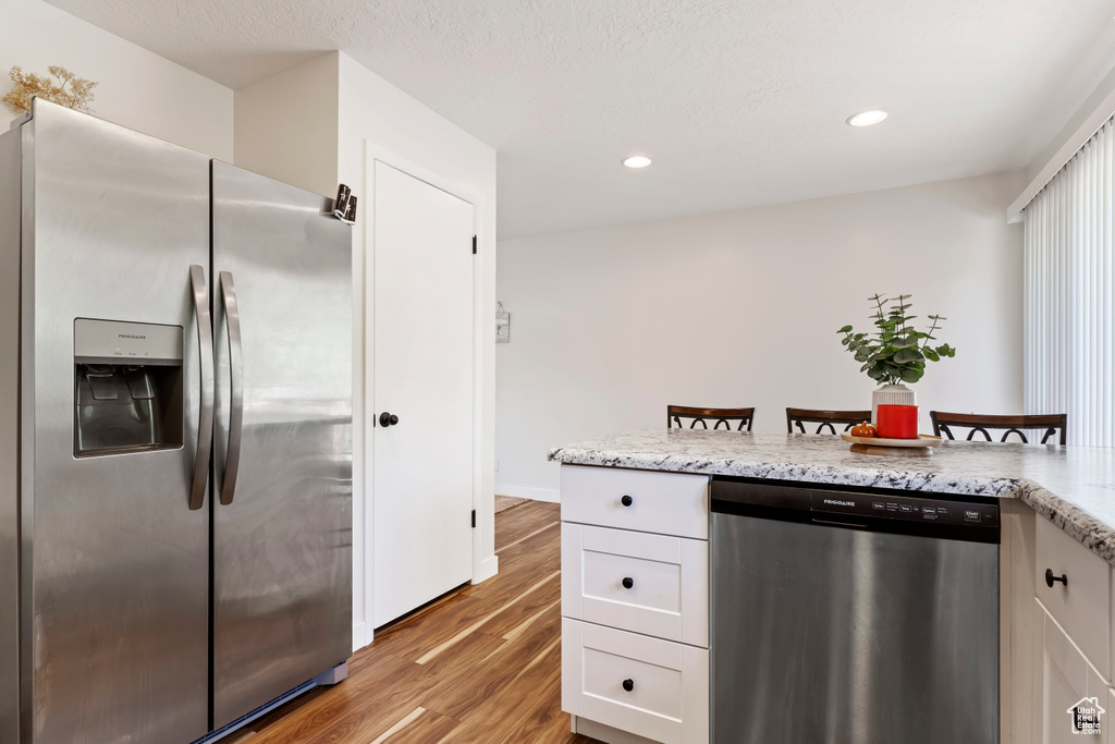 Kitchen with recessed lighting, white cabinetry, light stone countertops, light wood-style floors, and stainless steel appliances
