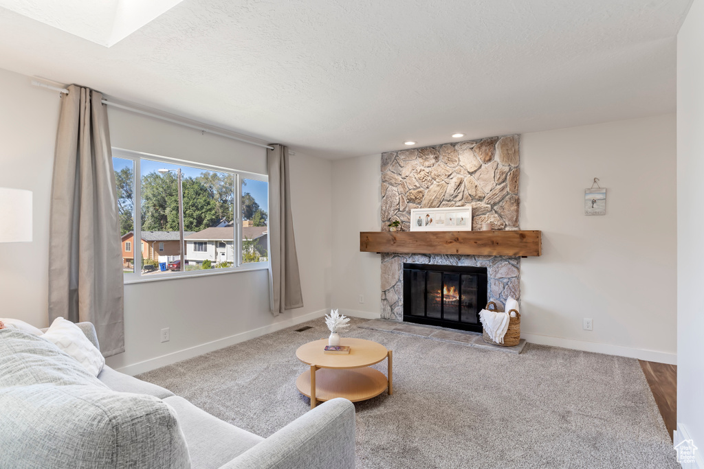 Carpeted living room with visible vents, baseboards, a textured ceiling, a fireplace, and recessed lighting
