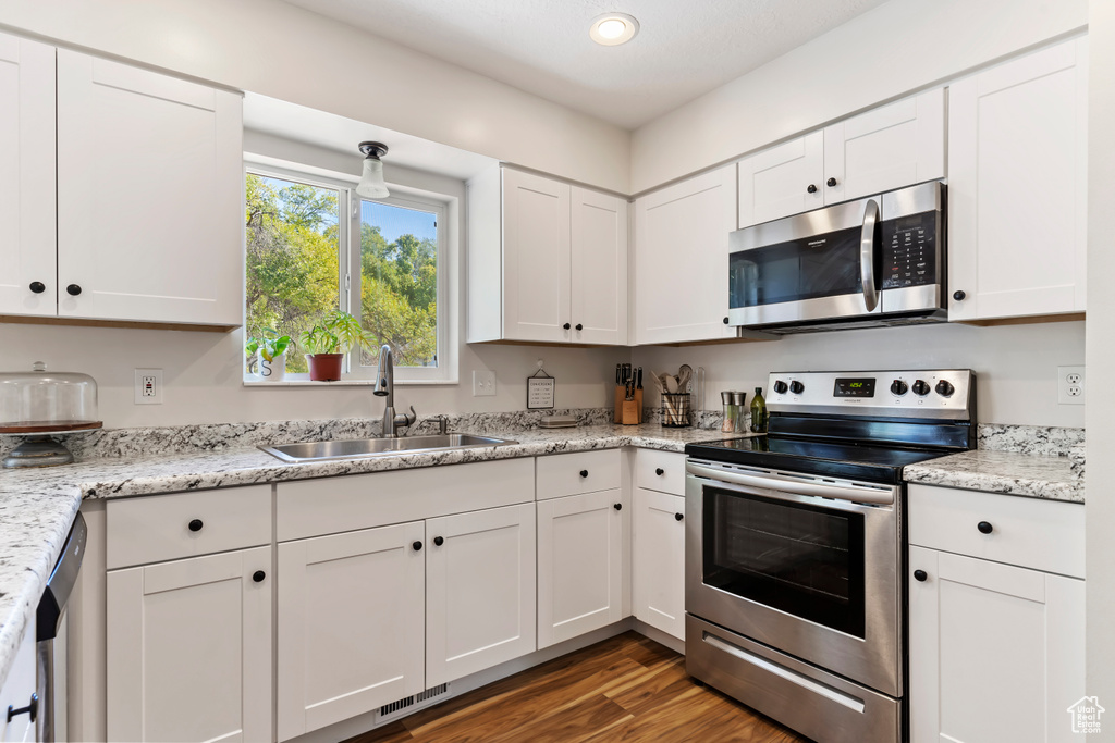 Kitchen with dark wood-style floors, white cabinets, visible vents, stainless steel appliances, and a sink