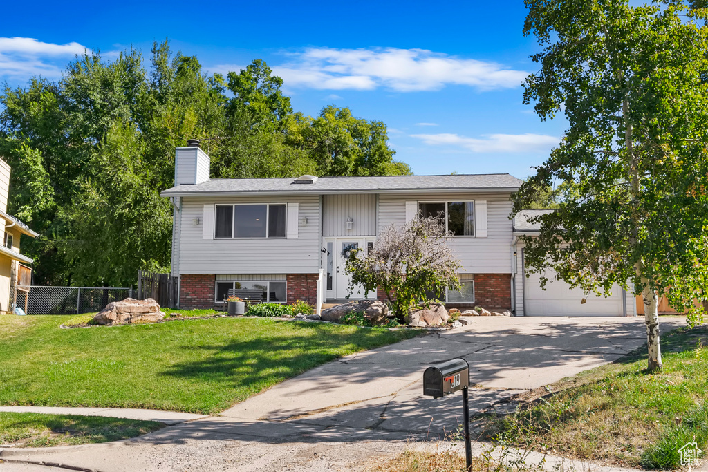 Split foyer home with a garage, a front lawn, brick siding, a chimney, and driveway
