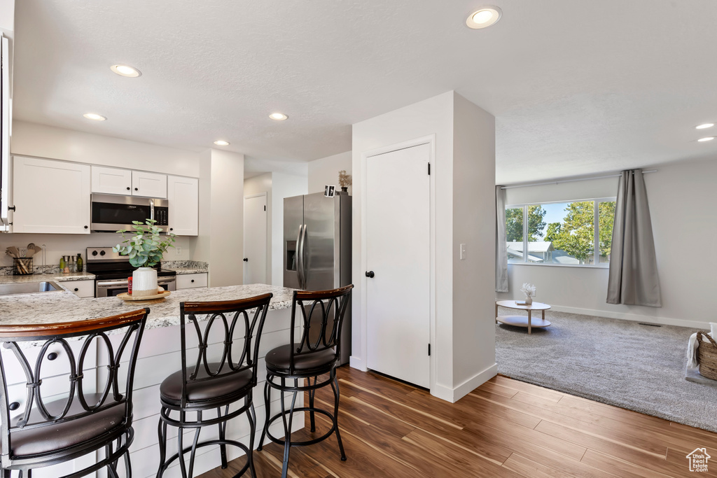 Kitchen with white cabinets, a kitchen bar, a peninsula, recessed lighting, and stainless steel appliances
