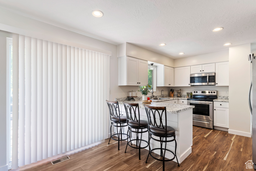 Kitchen featuring a kitchen bar, a peninsula, appliances with stainless steel finishes, and dark wood-type flooring