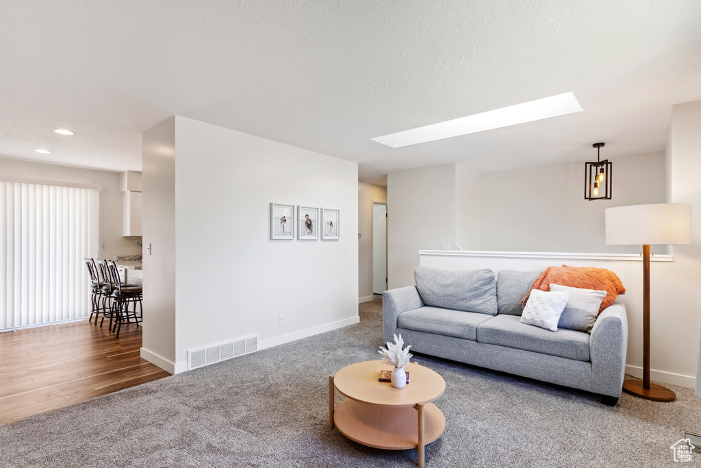 Carpeted living area featuring visible vents, baseboards, recessed lighting, wood finished floors, and a skylight