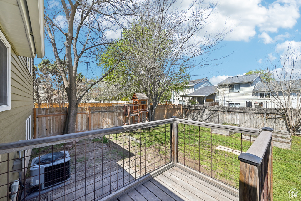 Wooden deck featuring cooling unit, a fenced backyard, a lawn, a playground, and a residential view