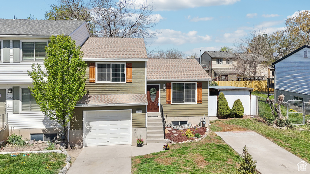 View of front facade with a shingled roof, driveway, fence, and an attached garage