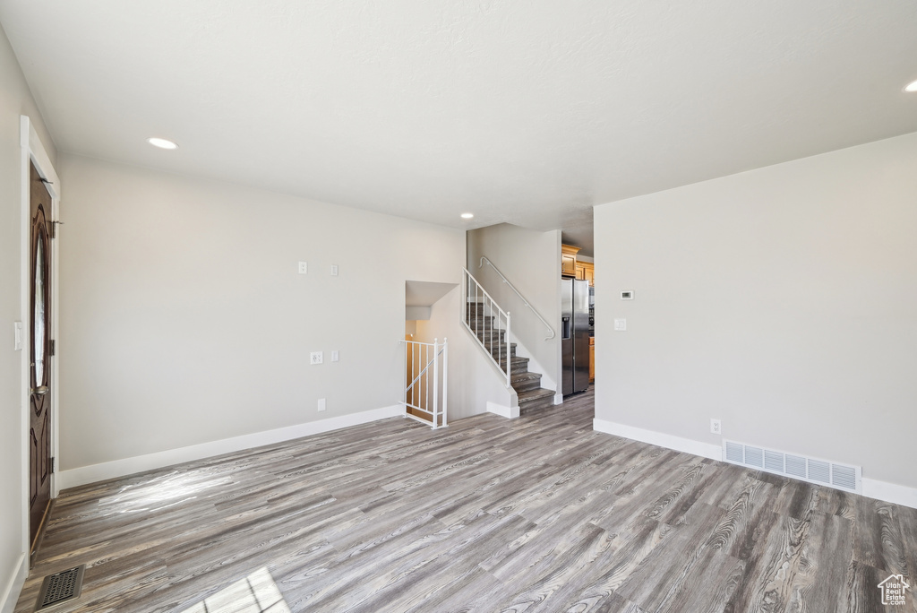 Unfurnished living room with wood finished floors, baseboards, visible vents, and stairway