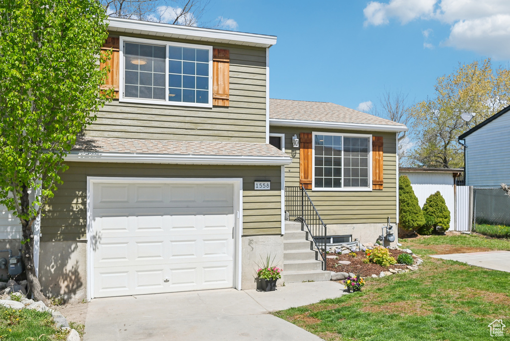Tri-level home featuring an attached garage, fence, a shingled roof, and concrete driveway