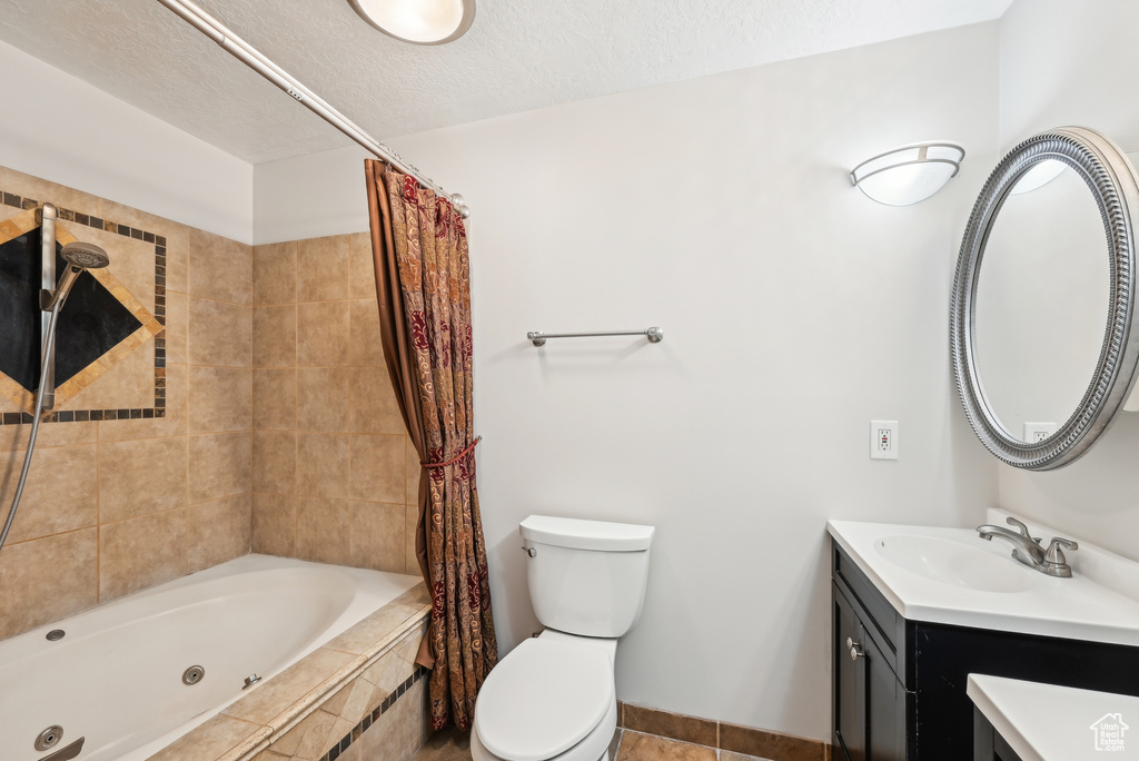 Full bath with a combined bath / shower with jetted tub, a textured ceiling, vanity, toilet, and tile patterned floors