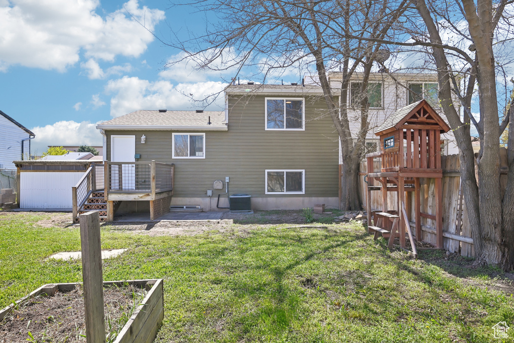 Rear view of property with central AC, a vegetable garden, fence, and a lawn