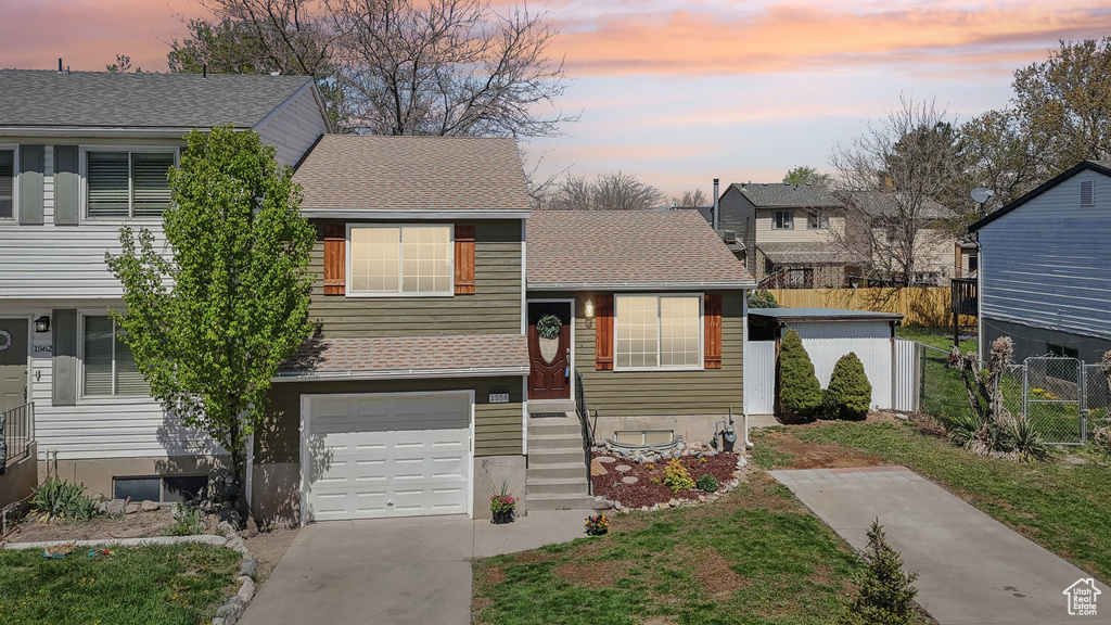 Tri-level home with driveway, fence, a shingled roof, and a garage