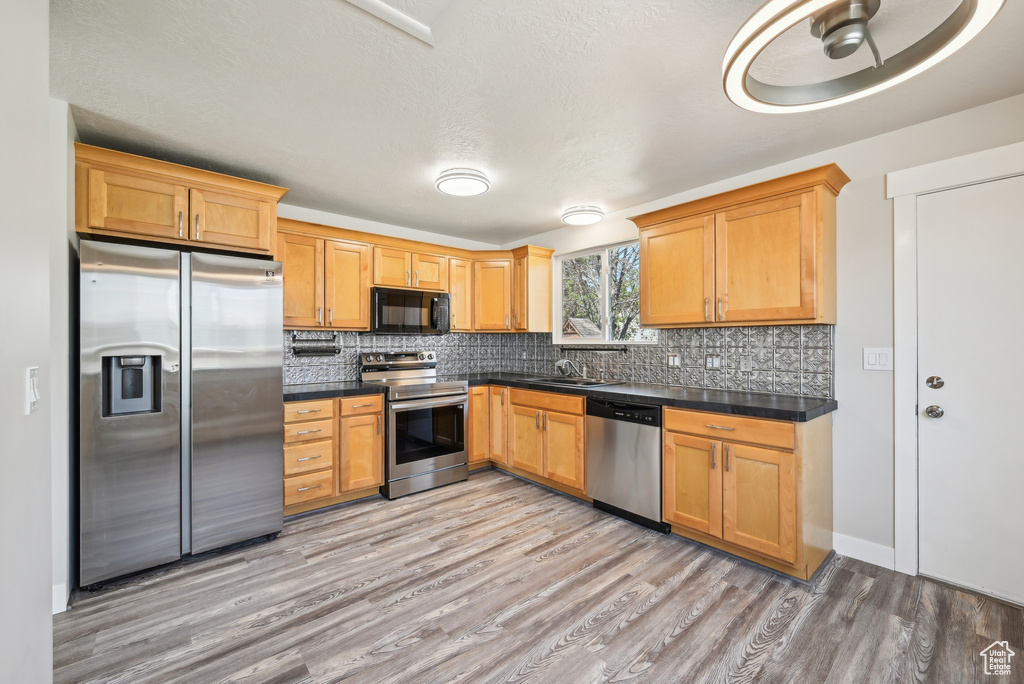 Kitchen featuring backsplash, dark countertops, appliances with stainless steel finishes, light wood finished floors, and a sink