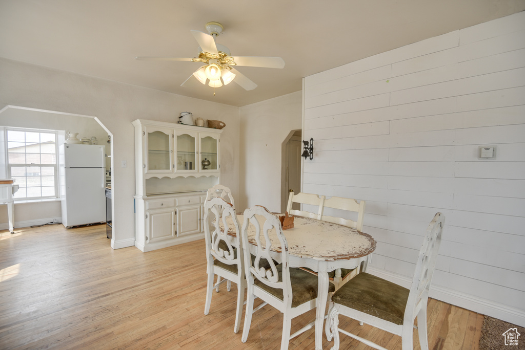 Dining space with ceiling fan, light wood finished floors, arched walkways, and baseboards