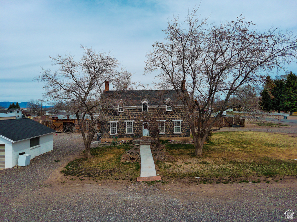 Cape cod house featuring a chimney, stone siding, and a front lawn