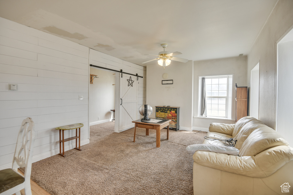 Living room featuring carpet floors, baseboards, a ceiling fan, and a barn door