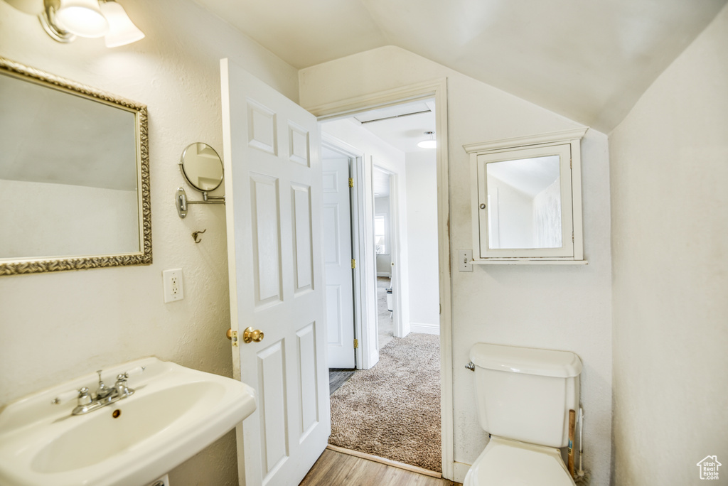Bathroom featuring toilet, wood finished floors, a sink, and vaulted ceiling