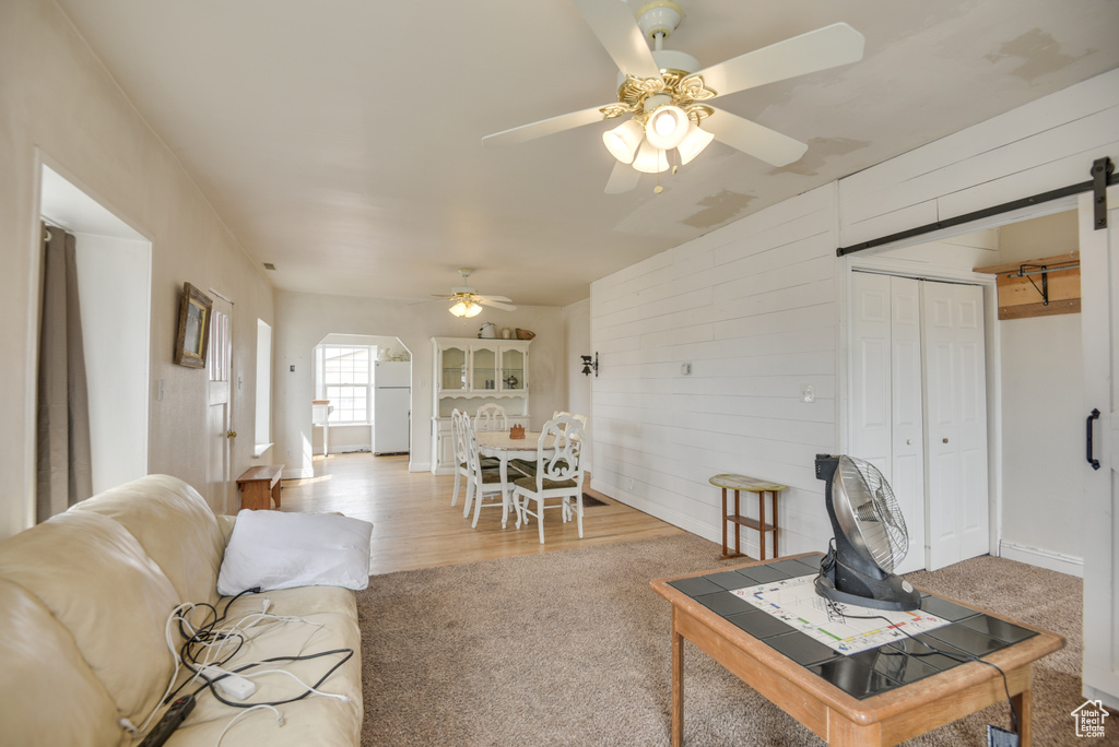 Carpeted living area featuring wooden walls, ceiling fan, arched walkways, and a barn door