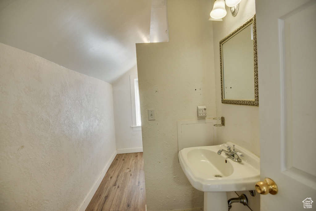 Bathroom with baseboards, vaulted ceiling, a textured wall, a sink, and wood finished floors